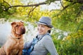 Happy young woman in a hat with dog Shar Pei sitting in the field in golden sunset light, true friends forever