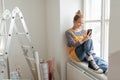 Happy young woman having break during renovation her aparatment. Using phone, searching inspiration at social medias. Royalty Free Stock Photo