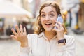 Happy young woman having remote conversation talking on smartphone, good news gossip in city street Royalty Free Stock Photo