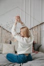 Happy young woman in headphones listening to music from smartphone and dancing on bed at home.