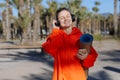 Happy young woman In headphones with yoga mat, listens music on smartphone outdoors. Smiling girl with closed eyes in Royalty Free Stock Photo