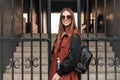 Happy young woman hipster with cute smile in stylish sunglasses in trendy casual youth clothes with leather backpack rests and Royalty Free Stock Photo