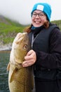 Happy young woman holding big arctic cod. Norway happy fishing. Fisherwoman with cod fish in hands Royalty Free Stock Photo