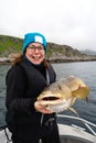 Happy young woman holding big arctic cod. Norway happy fishing. Fisherwoman with cod fish in hands Royalty Free Stock Photo