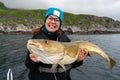 Happy young woman holding big arctic cod. Norway happy fishing. Fisherwoman with cod fish in hands Royalty Free Stock Photo