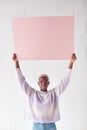 Happy Young Woman Holding Blank Pink Card With Copy Space Above Head White Against White Studio Wall