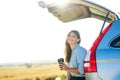 happy young woman holding coffee cup and sitting on the open trunk of her car in a wheat field at sunset Royalty Free Stock Photo