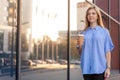 Happy young woman holding a coffee to go in disposable cup, walking along office Royalty Free Stock Photo