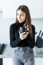 Happy young woman holding a cup of coffee in her kitchen