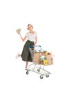 happy young woman holding dollar banknotes and standing with shopping trolley full of grocery Royalty Free Stock Photo