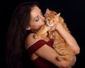Happy young woman holding on the hands her red maine coon kitten and kissing. Closeup portrait on black Royalty Free Stock Photo