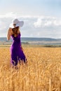 Happy young woman holding hat, walking in the golden wheat field. Sunset light. Summer nature. Royalty Free Stock Photo