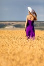 Happy young woman holding hat, walking in the golden wheat field. Sunset light. Summer nature. Royalty Free Stock Photo