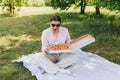Happy young woman holding hot pizza in box on nature background. Attractive girl feels hungry and loves the taste