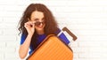 Happy young woman holding orange suitcase, going on a trip. Beautiful girl wearing sunglasses before traveling. Lifestyle and Royalty Free Stock Photo