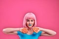 Happy young woman holding oranges halves on a pink background