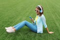 Happy young woman holding phone listening to music in headphones lying on grass in summer park Royalty Free Stock Photo