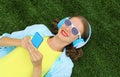 Happy young woman holding phone listening to music in headphones lying on grass in summer park Royalty Free Stock Photo