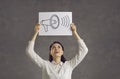 Happy young woman holding a sheet of paper with a picture of a yelling megaphone Royalty Free Stock Photo