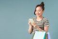 Happy young woman holding shopping bags and mobile phone over light blue background Royalty Free Stock Photo