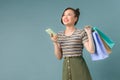 Happy young woman holding shopping bags and mobile phone over light blue background Royalty Free Stock Photo