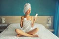 Happy young woman holding smartphone enjoying with cup of coffee drying her wet hair after bath with wrapped towel on her head Royalty Free Stock Photo