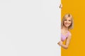 Happy young woman holding white advertising board, looking out of blank placard over yellow studio background, panorama Royalty Free Stock Photo