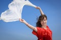 Happy young woman holding white scarf with opened arms expressing freedom, outdoor shot against blue sky Royalty Free Stock Photo