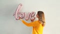 Happy young woman holding word love, letters shaped foil balloons on the wall Royalty Free Stock Photo