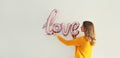 Happy young woman holding word love, letters shaped foil balloons on the wall Royalty Free Stock Photo