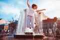 Happy young woman jumping by fountain on summer street