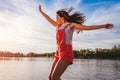 Happy young woman jumping and raising arms on river at sunset. Freedom. Active lifestyle