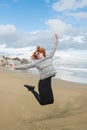 happy young woman jumping on seashore on cloudy day