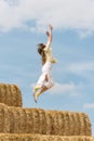 Happy young woman jumps from high haystack. Carefree girl has fun on the farm on blue sky background Royalty Free Stock Photo