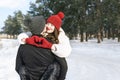 Happy young woman keeps hands in heart shape and embrace her boyfriend. Young loving couple in winter forest. Sunny day Royalty Free Stock Photo