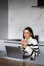 Happy young woman in the kitchen reading he news on her laptop Royalty Free Stock Photo