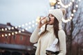 Happy young woman in knitted sweater and hat is going skating and drinks coffee