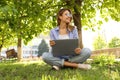 Happy young woman with laptop sitting on green grass in park Royalty Free Stock Photo