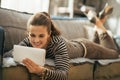 Happy young woman laying on couch and using tablet Royalty Free Stock Photo