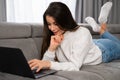 Happy young woman laying on sofa at home and looking on the laptop screen