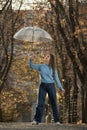 Happy young woman with long hair walks in autumn park. Beautiful girl with transparent umbrella