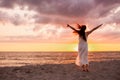 Happy young woman in a long white dress looking at the sunset on empty sand beach with her hands up. Freedoom, vacation Royalty Free Stock Photo