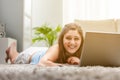 Happy young woman lying on a carpet with a laptop