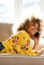 Happy young woman lying on couch at home talking with mobile phone Royalty Free Stock Photo