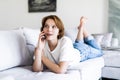 Happy young woman lying on the couch at home, talking on the phone with friend Royalty Free Stock Photo
