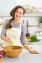 Happy young woman making salad in kitchen Royalty Free Stock Photo
