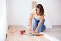 Happy young woman measuring and marking laminate floor tile for cutting