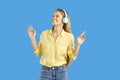 Happy young woman with modern stereo headphones enjoys her favorite music on light blue background. Royalty Free Stock Photo