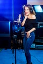 Happy young woman in the music studio with microphone and headphones wearing modern jeans and a black sweater Royalty Free Stock Photo