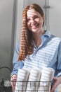 Happy young woman is neatly placing rolled up white towels into a metal mesh basket near bath sink. Royalty Free Stock Photo